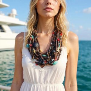 “Model wearing handcrafted Calypso Necklace with layered wood beads, turquoise stones, and coral accents against ocean backdrop.”