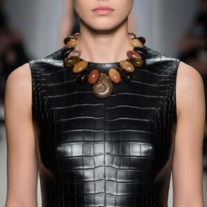Model wearing Rusty Necklace with Tiger Eye, Aventurine, and Ammonite fossil centerpiece styled over black textured leather dress.