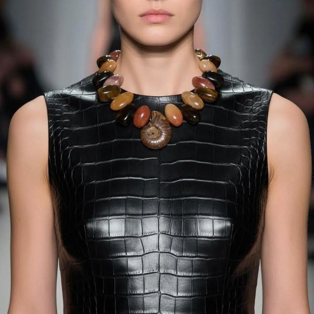 Model wearing Rusty Necklace with Tiger Eye, Aventurine, and Ammonite fossil centerpiece styled over black textured leather dress.