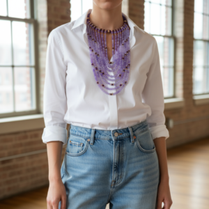 Model wearing multi‑strand purple glass bead necklace with brass accents styled over a white shirt and denim jeans.