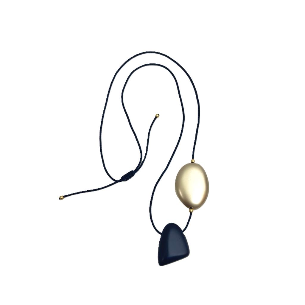 Long black cord necklace with matte black geometric pendant and gold oval accent on a white background.