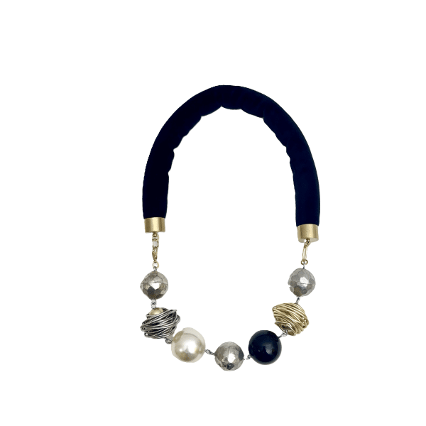Elevate your neckline with an exquisite balance of elegance and artistry. This black and white necklace features a luxurious black velvet cord adorned with a stunning array of mixed-shaped gold, silver, black, and pearl beads. Crafted to create the illusion of a longer neck, the beads’ strategic spacing guides the eye upward, accentuating the natural curve of the neckline. Each bead is selected for shape and hue, blending polished metallic tones with luminous pearls. The mix of onyx-like beads, shimmering silver, and warm gold produces an interplay of textures and light. Suspended on a soft velvet cord, the ensemble drapes gracefully, combining comfort and sophistication. Designed for versatility, this piece transitions effortlessly from day to evening attire. Pair it with a crisp white blouse to add modern refinement, or complement a little black dress for a timeless silhouette. Whether styled as a focal statement or layered with other necklaces, its refined geometry offers a flattering proportion that contributes to the illusion of elongation. Lightweight and comfortable, the velvet cord secures with a discreet clasp for a perfect fit. Let this piece blend classic black-and-white appeal with contemporary design. A testament to masterful craftsmanship, modern elegance. Embrace its transformative power and the third illusion it casts—elevating every ensemble with understated sophistication.