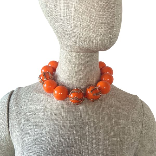 Statement Necklace with Gold Accents – 18" Acrylic Beads Bold, radiant, and full of personality, this statement necklace is crafted from large, glossy acrylic beads in a vivid Orange hue. Measuring 18 inches in length and weighing 8 ounces, it offers a substantial yet comfortable presence that instantly elevates any outfit. Three of the beads are adorned with intricate gold-toned accents, adding a touch of elegance and visual contrast to the vibrant color palette. The necklace is secured with a gold-colored toggle clasp that complements the gold detailing on the beads, creating a cohesive and polished finish.  Perfect for those who love bold accessories with refined details, this piece brings warmth and sophistication to both casual and formal looks. Whether worn solo or layered with other textures, it delivers a confident splash of Orange that feels both modern and timeless. The combination of smooth acrylic, metallic accents, and thoughtful design makes this necklace a standout addition to any jewelry collection.