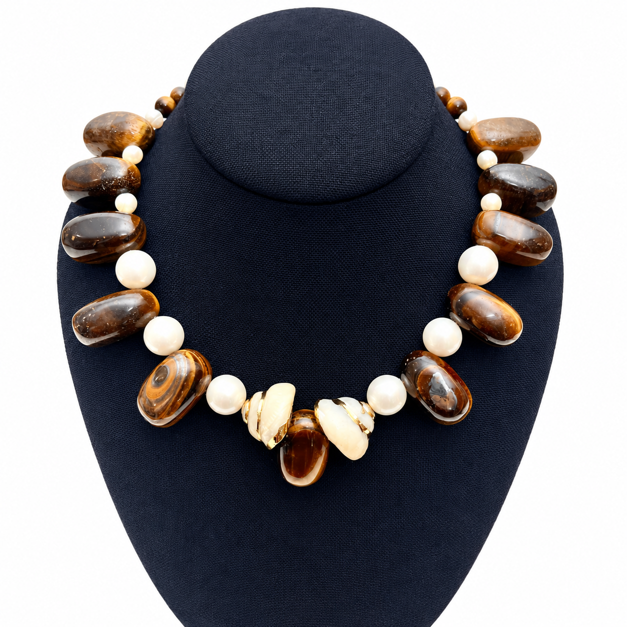 Handcrafted necklace displayed on a black jewelry bust featuring oval tiger eye stones with golden‑brown chatoyant bands, accented by white pearls and shell elements.
