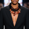 Model wearing a black tailored blazer and a bold velvet cord necklace with dangling red jasper stones, showcasing earthy tones and sculptural elegance.