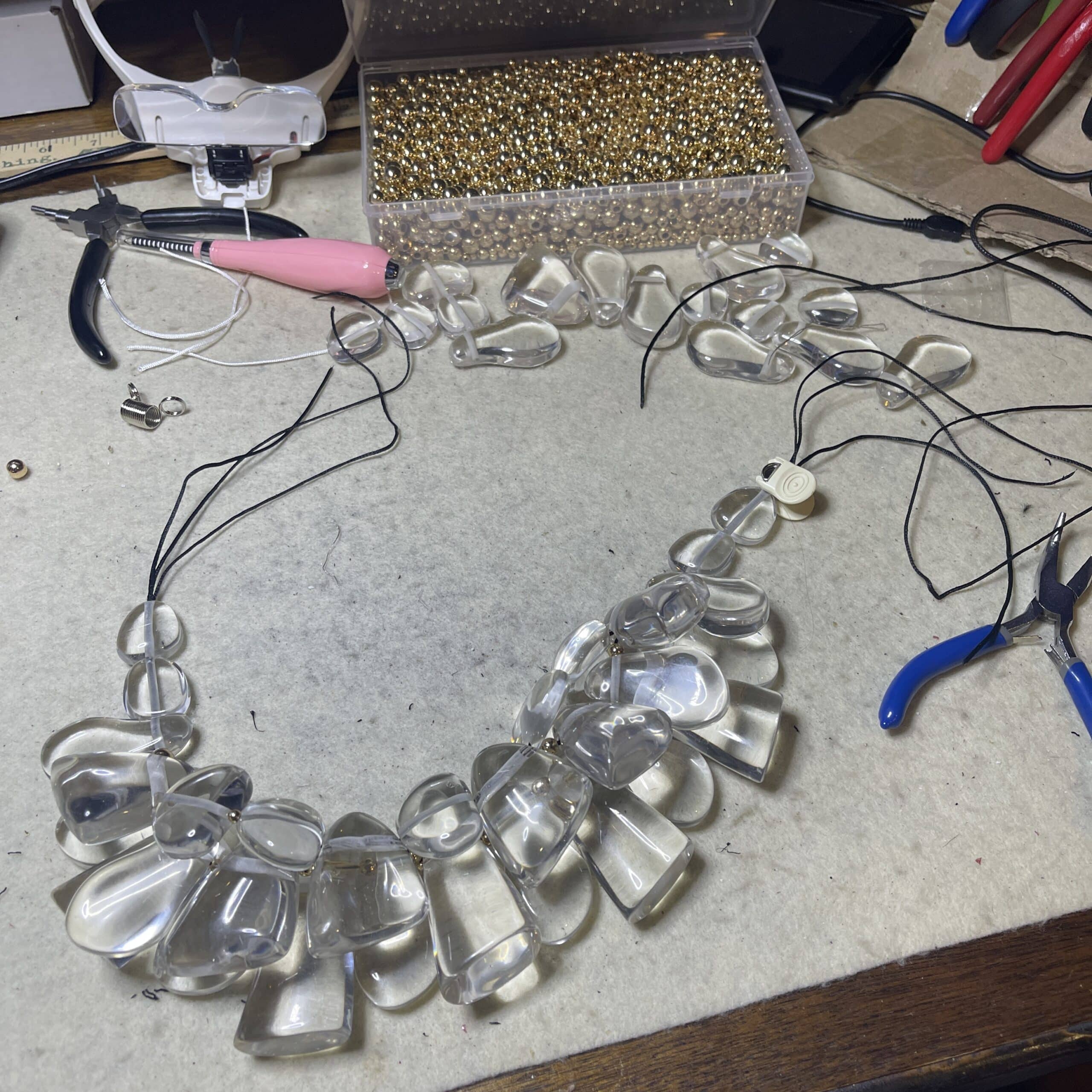 Clear Acrylic Cluster Necklace with Gold Accents Make a bold impression with this sculptural statement necklace, designed to evoke the crystalline beauty of ice.  Featuring a clustered arrangement of three strands of large, clear acrylic beads, this piece catches and reflects light with dazzling clarity.  Each bead is separated by gold-tone spacer accents, adding warmth and contrast to the cool, glass-like shimmer.   The necklace is secured with a large, easy-to-use lobster clasp, ensuring both comfort and durability. Measuring 17 inches in length with an adjustable extension up to 22 inches, it offers versatility for different necklines and styling preferences. At 16 ounces, it has a substantial feel—like wearing a piece of modern art. Whether you're dressing for a gallery opening, a winter soirée, or want to elevate your everyday look, this necklace will turn heads.  Its unique design mimics the elegance of ice formations, while the gold accents lend a touch of luxury.  This is more than jewelry—it’s a wearable sculpture, crafted to impress and inspire.  With its ice-like clarity and bold silhouette, it’s the perfect fusion of art and fashion.