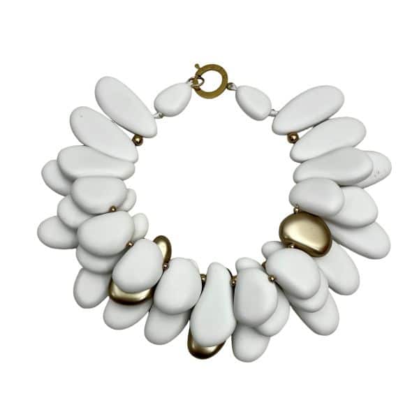 Winter White & Gold Acrylic Bead Necklace Command attention with this regal statement necklace, a sculptural blend of winter white and gleaming gold accents. Crafted with multilayered strands of acrylic beads, the design evokes natural pebbles—smooth, matte, and artfully arranged.  Interspersed among the white beads are gold-toned spacers, adding warmth and contrast to the cool palette. This necklace is more than an accessory—it’s a wearable art piece. The layered construction creates depth and movement, while the circular clasp ensures a secure and polished finish. Measuring 16 inches with an extension up to 21 inches, it adapts effortlessly to different necklines and occasions.  At 14 ounces, it has a bold, confident presence without compromising comfort. Whether paired with a crisp blouse or a dramatic evening dress, this necklace transitions seamlessly from day to night. Its regal tones and organic shapes make it a standout piece for gallery events, holiday gatherings, or everyday elegance. Celebrate your individuality with a design that’s both modern and timeless. The regal interplay of white and gold speaks to strength, grace, and artistic flair—perfect for those who love jewelry that makes a statement.