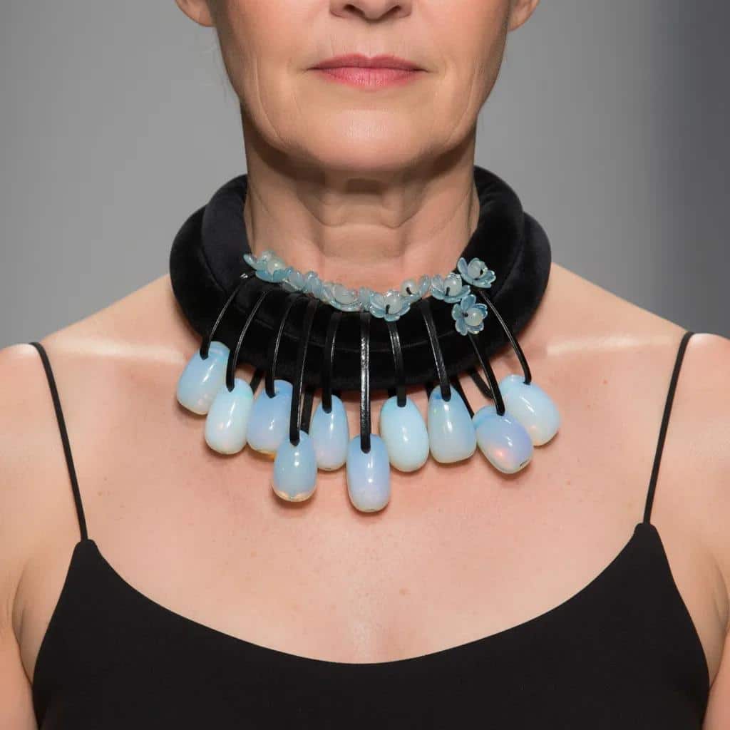 Translucent Opalite Velvet Choker Necklace Step into the light with this mesmerizing choker necklace, where translucent beauty meets bold design.  Featuring large, dangling Opalite beads suspended from a double velvet cord, this piece is crafted to capture attention.  Each bead is translucent, allowing light to pass through and dance across its surface, creating a subtle shimmer that shifts between blue and green tones depending on your surroundings. The dual velvet strands offer a rich, tactile contrast to the glass-like beads, enhancing the necklace’s visual depth and luxurious feel. Whether worn with a plunging neckline or layered over a high collar, this choker adds a touch of ethereal elegance to any outfit. • 💎 Materials: Translucent Opalite beads, soft velvet cord • 🎨 Color: Shifting hues of blue and green, influenced by ambient light • 🔗 Design: Double velvet cord with symmetrical dangling beads • 🌟 Style: Statement choker with a modern, mystical edge Perfect for evening wear, artistic ensembles, or everyday magic, this necklace invites compliments and conversation. The translucent nature of Opalite makes each piece feel alive—responding to light, mood, and movement. Let your jewelry reflect your radiance. This choker isn’t just an accessory—it’s a luminous expression of your unique style.  The necklace's weight is 9OZ, and 18IN long.