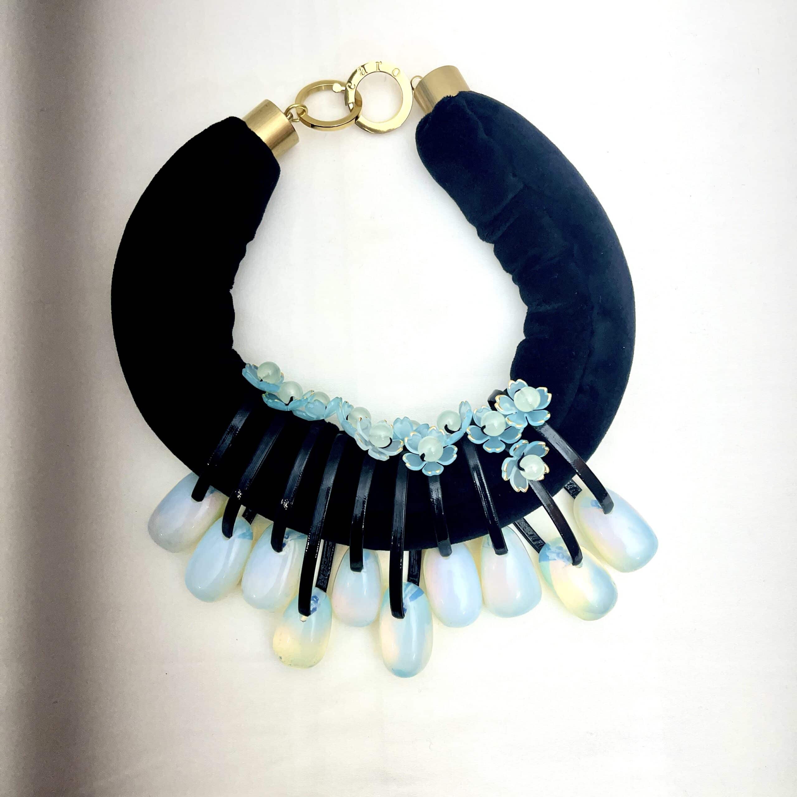 Translucent Opalite Velvet Choker Necklace Step into the light with this mesmerizing choker necklace, where translucent beauty meets bold design.  Featuring large, dangling Opalite beads suspended from a double velvet cord, this piece is crafted to capture attention.  Each bead is translucent, allowing light to pass through and dance across its surface, creating a subtle shimmer that shifts between blue and green tones depending on your surroundings. The dual velvet strands offer a rich, tactile contrast to the glass-like beads, enhancing the necklace’s visual depth and luxurious feel. Whether worn with a plunging neckline or layered over a high collar, this choker adds a touch of ethereal elegance to any outfit. • 💎 Materials: Translucent Opalite beads, soft velvet cord • 🎨 Color: Shifting hues of blue and green, influenced by ambient light • 🔗 Design: Double velvet cord with symmetrical dangling beads • 🌟 Style: Statement choker with a modern, mystical edge Perfect for evening wear, artistic ensembles, or everyday magic, this necklace invites compliments and conversation. The translucent nature of Opalite makes each piece feel alive—responding to light, mood, and movement. Let your jewelry reflect your radiance. This choker isn’t just an accessory—it’s a luminous expression of your unique style.  The necklace's weight is 9OZ, and 18IN long.