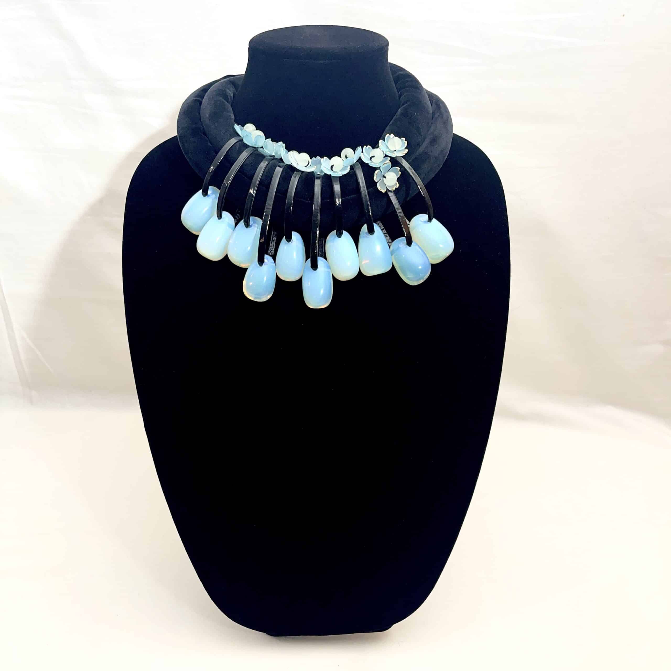 Translucent Opalite Velvet Choker Necklace Step into the light with this mesmerizing choker necklace, where translucent beauty meets bold design.  Featuring large, dangling Opalite beads suspended from a double velvet cord, this piece is crafted to capture attention.  Each bead is translucent, allowing light to pass through and dance across its surface, creating a subtle shimmer that shifts between blue and green tones depending on your surroundings. The dual velvet strands offer a rich, tactile contrast to the glass-like beads, enhancing the necklace’s visual depth and luxurious feel. Whether worn with a plunging neckline or layered over a high collar, this choker adds a touch of ethereal elegance to any outfit. • 💎 Materials: Translucent Opalite beads, soft velvet cord • 🎨 Color: Shifting hues of blue and green, influenced by ambient light • 🔗 Design: Double velvet cord with symmetrical dangling beads • 🌟 Style: Statement choker with a modern, mystical edge Perfect for evening wear, artistic ensembles, or everyday magic, this necklace invites compliments and conversation. The translucent nature of Opalite makes each piece feel alive—responding to light, mood, and movement. Let your jewelry reflect your radiance. This choker isn’t just an accessory—it’s a luminous expression of your unique style.  The necklace's weight is 9OZ, and 18IN long.