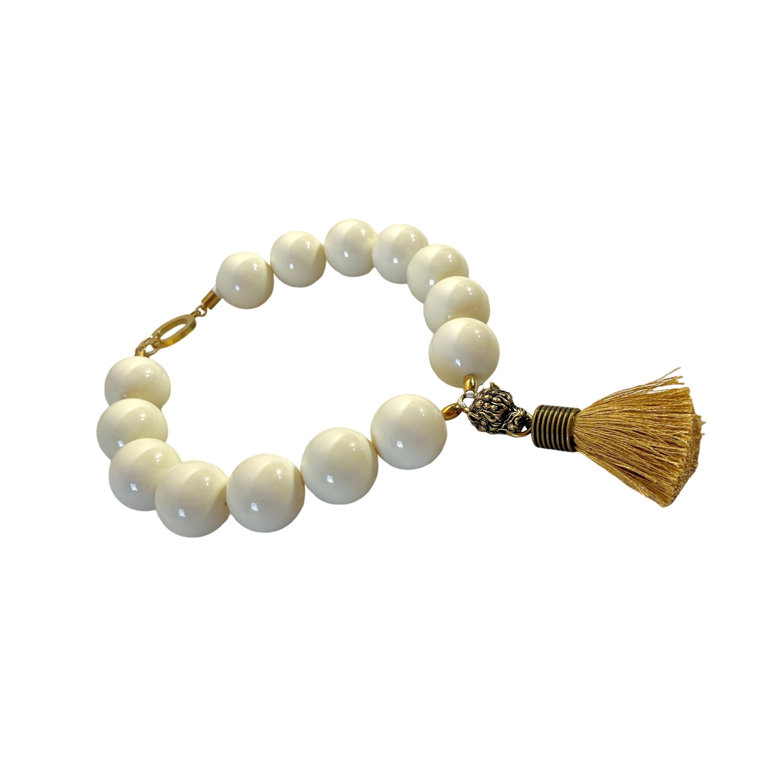 Elevate your style with this bold and elegant choker necklace, crafted from large cream-colored beads that exude timeless sophistication.  Measuring 19 inches in length and weighing 9 ounces, this statement piece balances substantial presence with refined detail.  Each glossy bead is carefully arranged to create a harmonious circular silhouette, anchored by a striking Mastiff pendant that commands attention. The pendant features a regal Mastiff motif, sculpted with intricate detail and finished in a rich gold tone.  From its mouth hangs a luxurious tassel, adding movement and texture to the design.  This symbolic centerpiece evokes strength, loyalty, and grace—perfect for those who appreciate jewelry with meaning. A large lobster clasp ensures secure fastening and ease of wear, while complementing the necklace’s bold aesthetic.  Whether paired with evening attire or used to elevate a casual ensemble, this choker offers versatility and impact. Designed for those who embrace powerful accessories, the Mastiff pendant serves as both a focal point and a conversation starter.  Let it reflect your inner strength and refined taste.  Crafted to leave a lasting impression.