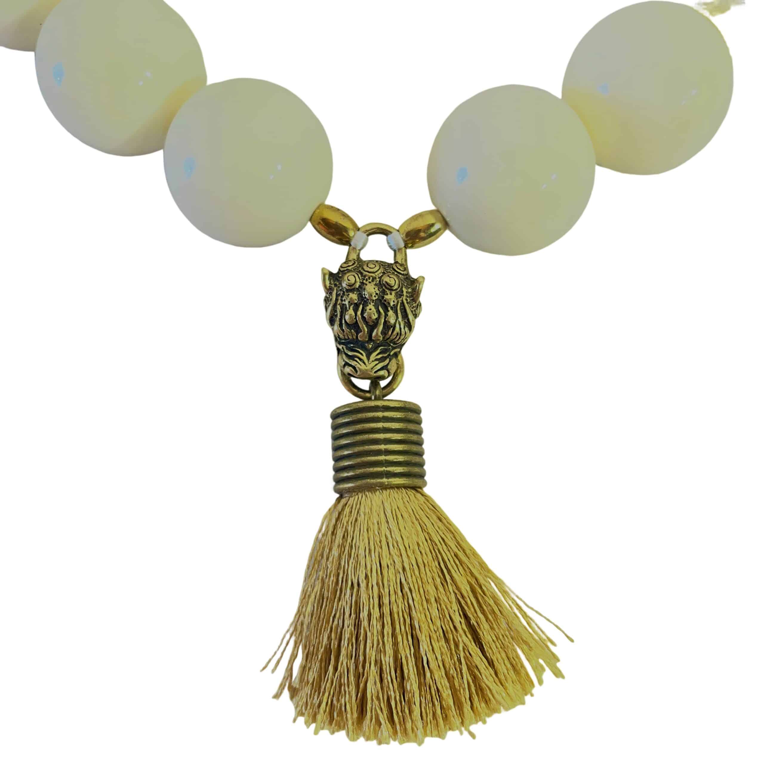 Elevate your style with this bold and elegant choker necklace, crafted from large cream-colored beads that exude timeless sophistication.  Measuring 19 inches in length and weighing 9 ounces, this statement piece balances substantial presence with refined detail.  Each glossy bead is carefully arranged to create a harmonious circular silhouette, anchored by a striking Mastiff pendant that commands attention. The pendant features a regal Mastiff motif, sculpted with intricate detail and finished in a rich gold tone.  From its mouth hangs a luxurious tassel, adding movement and texture to the design.  This symbolic centerpiece evokes strength, loyalty, and grace—perfect for those who appreciate jewelry with meaning. A large lobster clasp ensures secure fastening and ease of wear, while complementing the necklace’s bold aesthetic.  Whether paired with evening attire or used to elevate a casual ensemble, this choker offers versatility and impact. Designed for those who embrace powerful accessories, the Mastiff pendant serves as both a focal point and a conversation starter.  Let it reflect your inner strength and refined taste.  Crafted to leave a lasting impression.
