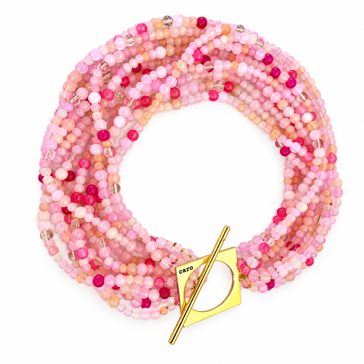 Multi-strand necklace made of small round glass beads in varying shades of pink, peach, and rose. The strands are twisted together into a thick rope-like form, secured by a large geometric gold toggle clasp engraved with “caro.” The design combines soft color gradients with a modern metallic accent.
