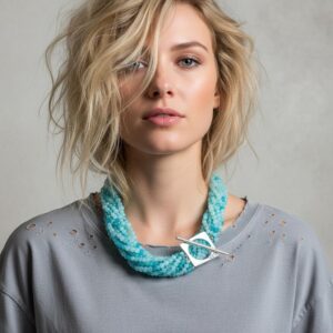 Model wearing a light gray top with small distressed details near the neckline, accessorized with a turquoise multi-strand beaded necklace featuring a bold silver geometric clasp. The necklace rests elegantly around the neck, adding a modern, artistic touch to the casual outfit.
