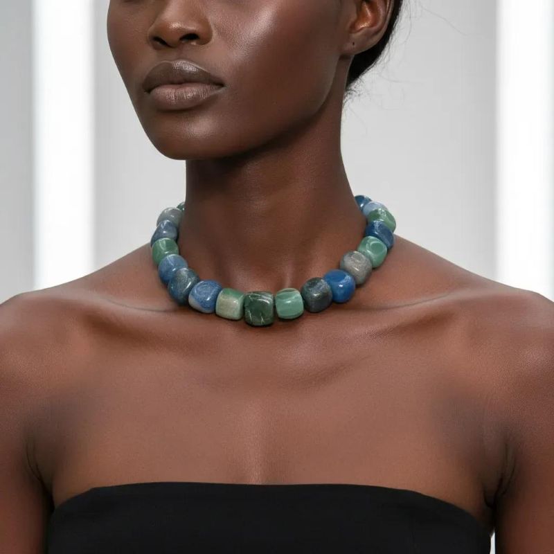 Naturale Aventurine Necklace Bold fortune, carved from the earth. This striking necklace is a celebration of Aventurine’s raw elegance and mythical charm. Composed of extra-large beads in rich shades of blue and green, each stone reveals its naturale character—swirls, flecks, and gradients formed over centuries. Unlike typical designs that rely on smaller, easier-to-drill beads, this piece defies convention. The hardiness of Aventurine makes large-scale craftsmanship a challenge, and that rarity is part of its allure. Measuring 18 inches, the necklace wears like a choker due to the generous size of the stones, but includes an extension to reach up to 22 inches for added versatility. The bold silhouette and saturated hues create a dramatic presence, ideal for those who favor statement pieces with soul. Aventurine is revered as a Lucky Talisman, believed to attract opportunity and shield against negativity. This necklace doesn’t just adorn—it empowers. Whether worn with minimalist attire or layered over textured fabrics, it commands attention while remaining grounded in its naturale origins. Let it be your daily armor or your ceremonial accent. With every bead, it whispers of resilience, beauty, and the quiet power of the naturale world.  **Please request a longer extension if you are ordering this necklace for a male.