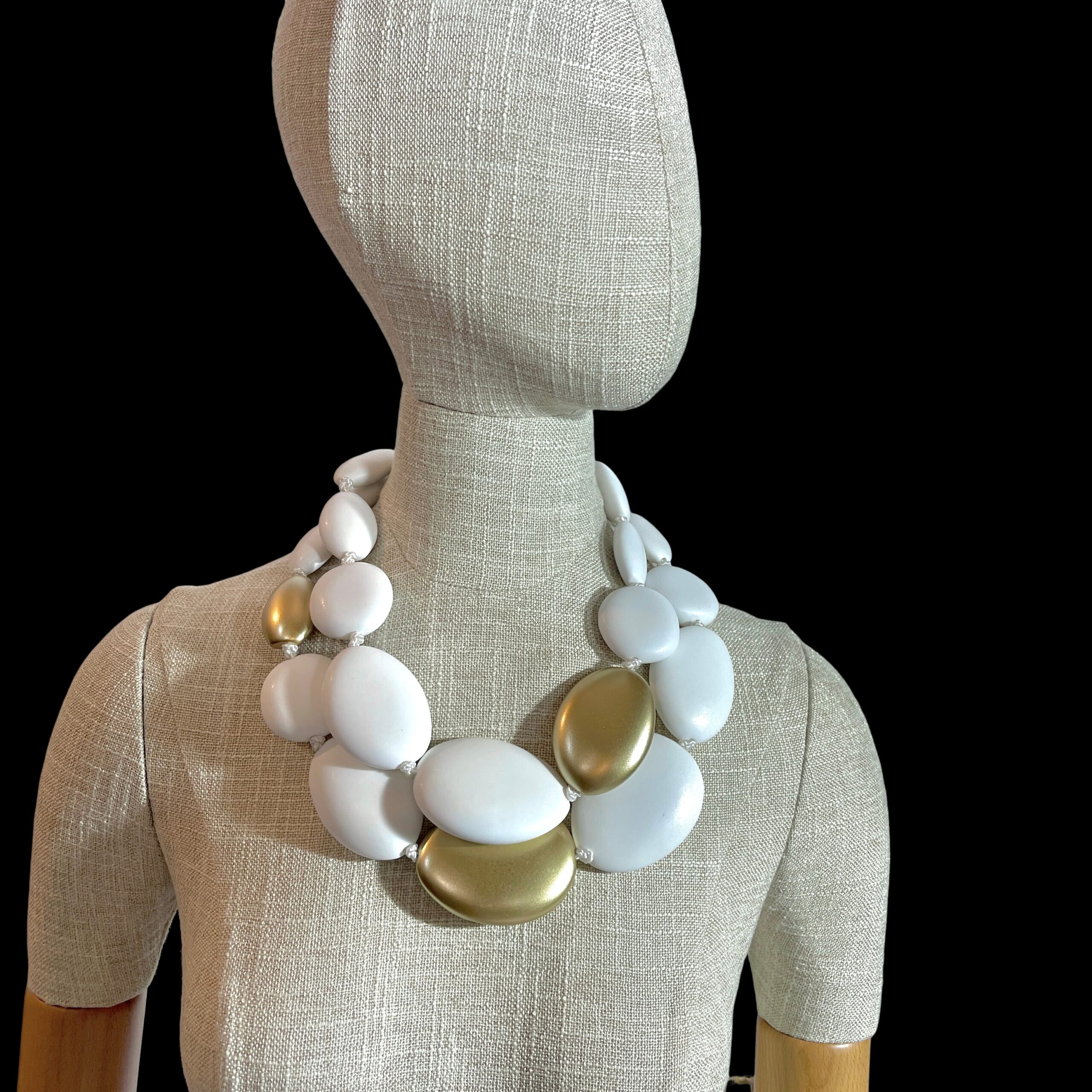 Double White Necklace – Bold Elegance in Every Curve Elevate your style with the Double White necklace, a striking statement piece that blends modern simplicity with timeless charm.  Crafted from two strands of oversized oval acrylic beads, this necklace offers a bold silhouette that catches the eye and complements any neckline.  The smooth, milky-white finish of each bead evokes purity and sophistication, while strategically placed gold accent beads add a touch of warmth and luxury. Designed for those who appreciate balance and contrast, the Double White necklace pairs effortlessly with both casual and formal attire.  Whether layered over a crisp blouse or worn with an evening dress, its dual-strand composition creates depth and movement, making it a versatile addition to your jewelry collection. A gold-toned spring ring clasp ensures secure wear and adds a refined finishing touch.  Lightweight yet impactful, this piece is ideal for all-day comfort without compromising on style.  The Double White necklace is more than an accessory—it’s a reflection of bold femininity and artistic flair. Perfect for gifting or personal indulgence, this necklace invites you to embrace elegance with a contemporary twist. Let your jewelry speak volumes—start with this unforgettable design.