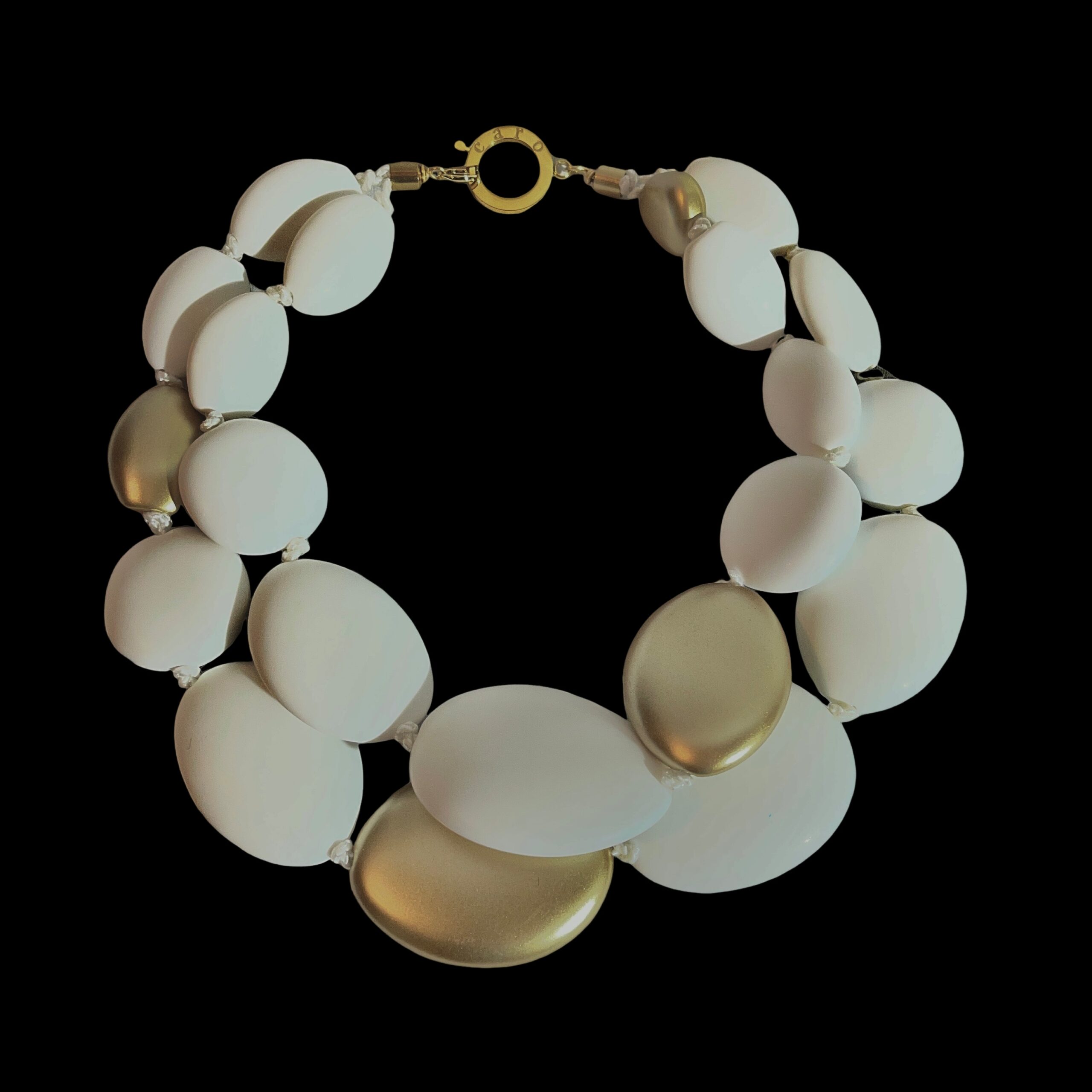 Double White Necklace – Bold Elegance in Every Curve Elevate your style with the Double White necklace, a striking statement piece that blends modern simplicity with timeless charm.  Crafted from two strands of oversized oval acrylic beads, this necklace offers a bold silhouette that catches the eye and complements any neckline.  The smooth, milky-white finish of each bead evokes purity and sophistication, while strategically placed gold accent beads add a touch of warmth and luxury. Designed for those who appreciate balance and contrast, the Double White necklace pairs effortlessly with both casual and formal attire.  Whether layered over a crisp blouse or worn with an evening dress, its dual-strand composition creates depth and movement, making it a versatile addition to your jewelry collection. A gold-toned spring ring clasp ensures secure wear and adds a refined finishing touch.  Lightweight yet impactful, this piece is ideal for all-day comfort without compromising on style.  The Double White necklace is more than an accessory—it’s a reflection of bold femininity and artistic flair. Perfect for gifting or personal indulgence, this necklace invites you to embrace elegance with a contemporary twist. Let your jewelry speak volumes—start with this unforgettable design.