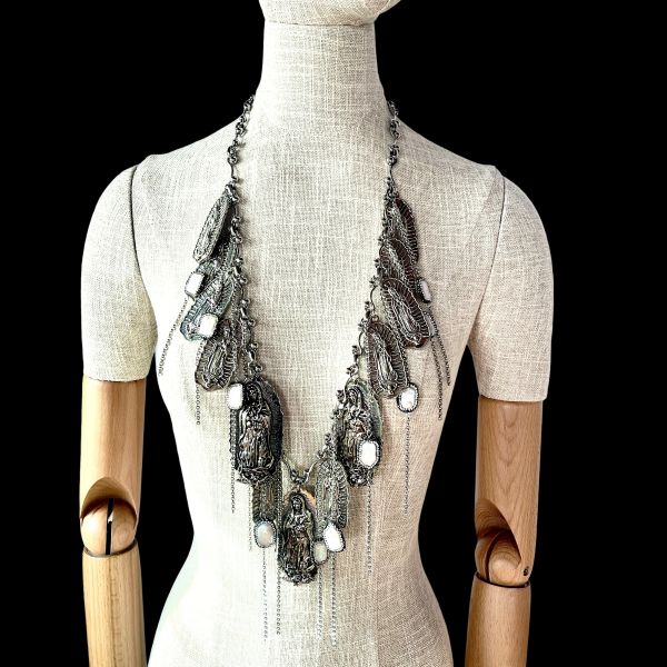 Reassurance Necklace Fierce elegance meets sacred rebellion. This 33-inch necklace is a visceral blend of armor and artistry. Heavy with intention at 14 oz, it drapes like a protective veil—layered silver-tone chains cascading with medallions that evoke mysticism and defiance. Fine threads of chain shimmer with freshwater pearls, softening the edge with quiet grace. Each element is chosen not just for beauty, but for symbolism: a chorus of metallic icons and sacred motifs that speak to resilience, identity, and unapologetic strength. Designed for those who walk the line between vulnerability and power, this piece commands attention. It pairs effortlessly with satin, leather, or bare skin—transforming any look into a statement. Whether worn solo or layered, it becomes a personal relic, a wearable manifesto. The Reassurance necklace doesn’t whisper. It roars. It’s for the ones who guard their hearts with style and speak their truth through adornment. It’s for the ones who know that protection can be beautiful, and beauty can be bold. Only one made. Details: Length: 33 inches Weight: 14 oz Materials: Silver-tone chain, freshwater pearls, mixed metal medallions Style: Rock & roll statement with symbolic depth Reassurance is not just jewelry. It’s armor with soul.