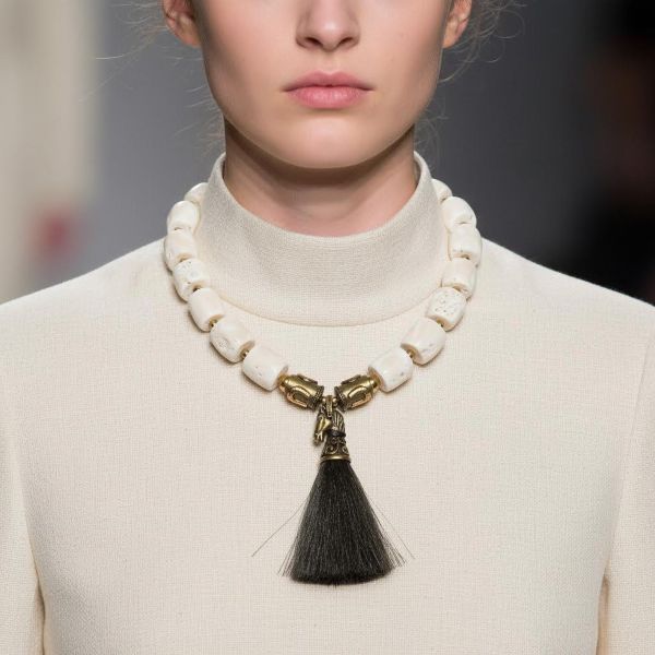 Horseshoe Necklace Where wild grace meets crafted power. This striking necklace blends equestrian spirit with artisanal elegance. Made of large, white natural coral beads and bold brass accents, it carries the weight of tradition and the freedom of open terrain. At 10 ounces and 19 inches long—extending to 24 inches—it drapes with confident presence, each element chosen for symbolism and strength. The clasp features horseshoe-adorned beads, a nod to protection and fortune. These same beads anchor the centerpiece: a finely sculpted brass horse head, detailed with reverence and crowned by a tassel of dark horsehair. It’s a tactile tribute to movement, loyalty, and untamed beauty. This piece isn’t just jewelry—it’s a talisman. A wearable homage to the bond between rider and steed, between earth and spirit. Whether paired with denim or silk, the Horseshoe necklace commands attention and tells a story of resilience, grace, and grounded elegance.  As the brass patina with time, it makes a better contrast with the white coral. Let the coral cool your skin. Let the brass catch the light. Let the Horseshoe guide your stride—three times over, in the language of adornment. Details: Length: 19–24 inches Weight: 10 oz Materials: Natural white coral, brass, horsehair tassel, horseshoe beads Style: Equestrian heritage statement piece