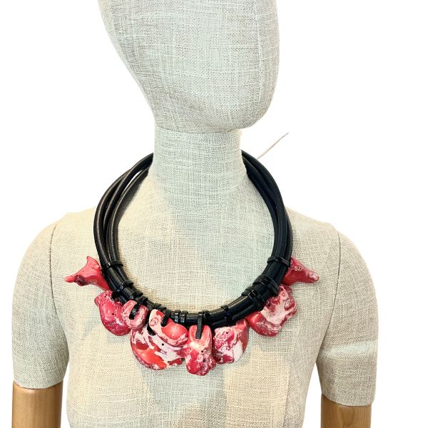 Rose Petals Necklace Where anatomy meets poetry, and coral blooms in motion. This bold, sculptural necklace is a celebration of organic form and emotional resonance. Crafted from sleek black cord and adorned with marbled red and white coral, each suspended stone evokes the delicate yet visceral beauty of rose petals—petals reimagined through texture, weight, and asymmetry. At 22 inches long and weighing 11 ounces, it rests with confident gravity, a wearable piece of art that speaks to both strength and sentiment. The coral charms, each uniquely shaped, sway like blossoms caught in a breeze. Their marbled surfaces suggest veins and movement, offering a tactile experience that’s both raw and refined. The black cord anchors the composition, providing contrast and structure, while allowing the stones to take center stage. This is not a necklace for the faint of heart. It’s for those who find beauty in imperfection, who wear emotion like armor, and who understand that adornment can be both provocative and poetic. Whether paired with minimalist attire or layered over bold textures, the Rose Petals necklace makes a statement that lingers. Let the stones speak. Let the cord hold. Let Rose Petals bloom—three times over, in the language of design. (This necklace is 22 inches, and it is not adjustable.) Details: Length: 22 inches Weight: 11 oz Materials: Black cord, marbled red and white coral Style: Avant-garde botanical statement piece