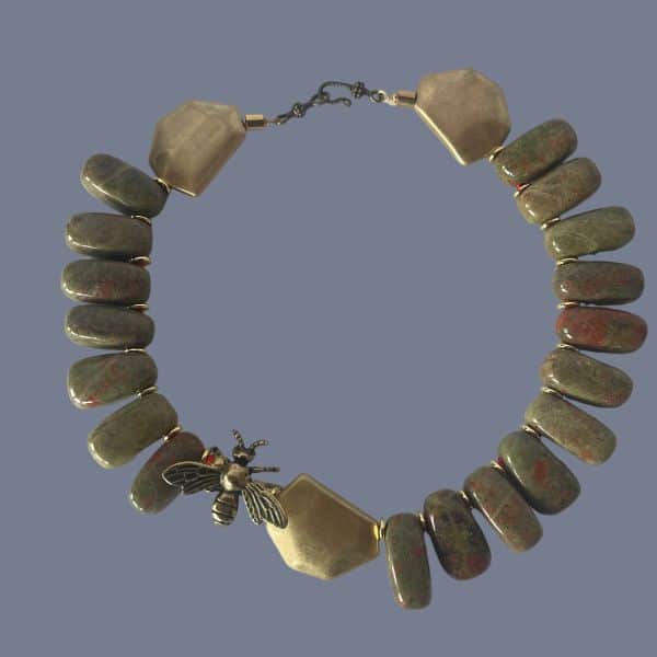 Honey 0369238 is crafted with reverence for nature and history. This 18-inch necklace is a tribute to the enduring beauty of the Appalachian landscape. Each polished Unakite bead—an earthy fusion of green epidote and pink feldspar—is carefully selected for its rich, mottled texture. The red pigments within the stone are thoughtfully echoed by the red cord threading the necklace, creating a warm, harmonious palette. Unakite was first discovered in the Great Smoky Mountains, a region steeped in Cherokee heritage and geological wonder, straddling western North Carolina and eastern Tennessee. Golden accent beads flank a central bee ornament, symbolizing industriousness and the sweetness of life. In ancient cultures, bees were revered as messengers between worlds and guardians of sacred knowledge. This piece channels that legacy, offering a wearable talisman of transformation and abundance. Weighing 12 ounces, the necklace carries a satisfying heft, grounding the wearer in both style and symbolism. Whether worn as a statement piece or a subtle nod to nature’s artistry, it evokes the golden warmth of Honey—its color, its spirit, and its timeless allure. Let this necklace be your daily drop of Honey, a reminder of the sweetness found in resilience, craftsmanship, and the quiet hum of history.