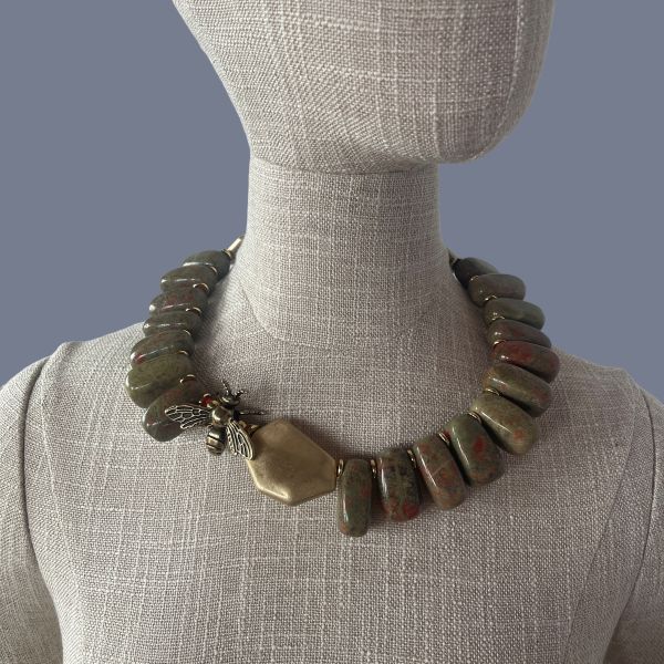 Honey 0369238 is crafted with reverence for nature and history. This 18-inch necklace is a tribute to the enduring beauty of the Appalachian landscape. Each polished Unakite bead—an earthy fusion of green epidote and pink feldspar—is carefully selected for its rich, mottled texture. The red pigments within the stone are thoughtfully echoed by the red cord threading the necklace, creating a warm, harmonious palette. Unakite was first discovered in the Great Smoky Mountains, a region steeped in Cherokee heritage and geological wonder, straddling western North Carolina and eastern Tennessee. Golden accent beads flank a central bee ornament, symbolizing industriousness and the sweetness of life. In ancient cultures, bees were revered as messengers between worlds and guardians of sacred knowledge. This piece channels that legacy, offering a wearable talisman of transformation and abundance. Weighing 12 ounces, the necklace carries a satisfying heft, grounding the wearer in both style and symbolism. Whether worn as a statement piece or a subtle nod to nature’s artistry, it evokes the golden warmth of Honey—its color, its spirit, and its timeless allure. Let this necklace be your daily drop of Honey, a reminder of the sweetness found in resilience, craftsmanship, and the quiet hum of history.