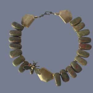 Honey 0369238 is crafted with reverence for nature and history. This 18-inch necklace is a tribute to the enduring beauty of the Appalachian landscape. Each polished Unakite bead—an earthy fusion of green epidote and pink feldspar—is carefully selected for its rich, mottled texture. The red pigments within the stone are thoughtfully echoed by the red cord threading the necklace, creating a warm, harmonious palette. Unakite was first discovered in the Great Smoky Mountains, a region steeped in Cherokee heritage and geological wonder, straddling western North Carolina and eastern Tennessee. Golden accent beads flank a central bee ornament, symbolizing industriousness and the sweetness of life. In ancient cultures, bees were revered as messengers between worlds and guardians of sacred knowledge. This piece channels that legacy, offering a wearable talisman of transformation and abundance. Weighing 12 ounces, the necklace carries a satisfying heft, grounding the wearer in both style and symbolism. Whether worn as a statement piece or a subtle nod to nature’s artistry, it evokes the golden warmth of Honey—its color, its spirit, and its timeless allure. Let this necklace be your daily drop of Honey, a reminder of the sweetness found in resilience, craftsmanship, and the quiet hum of history.