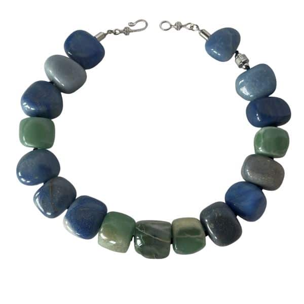 Naturale Aventurine Necklace Bold fortune, carved from the earth. This striking necklace is a celebration of Aventurine’s raw elegance and mythical charm. Composed of extra-large beads in rich shades of blue and green, each stone reveals its naturale character—swirls, flecks, and gradients formed over centuries. Unlike typical designs that rely on smaller, easier-to-drill beads, this piece defies convention. The hardiness of Aventurine makes large-scale craftsmanship a challenge, and that rarity is part of its allure. Measuring 18 inches, the necklace wears like a choker due to the generous size of the stones, but includes an extension to reach up to 22 inches for added versatility. The bold silhouette and saturated hues create a dramatic presence, ideal for those who favor statement pieces with soul. Aventurine is revered as a Lucky Talisman, believed to attract opportunity and shield against negativity. This necklace doesn’t just adorn—it empowers. Whether worn with minimalist attire or layered over textured fabrics, it commands attention while remaining grounded in its naturale origins. Let it be your daily armor or your ceremonial accent. With every bead, it whispers of resilience, beauty, and the quiet power of the naturale world.  **Please request a longer extension if you are ordering this necklace for a male.