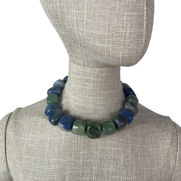 Naturale Aventurine Necklace Bold fortune, carved from the earth. This striking necklace is a celebration of Aventurine’s raw elegance and mythical charm. Composed of extra-large beads in rich shades of blue and green, each stone reveals its naturale character—swirls, flecks, and gradients formed over centuries. Unlike typical designs that rely on smaller, easier-to-drill beads, this piece defies convention. The hardiness of Aventurine makes large-scale craftsmanship a challenge, and that rarity is part of its allure. Measuring 18 inches, the necklace wears like a choker due to the generous size of the stones, but includes an extension to reach up to 22 inches for added versatility. The bold silhouette and saturated hues create a dramatic presence, ideal for those who favor statement pieces with soul. Aventurine is revered as a Lucky Talisman, believed to attract opportunity and shield against negativity. This necklace doesn’t just adorn—it empowers. Whether worn with minimalist attire or layered over textured fabrics, it commands attention while remaining grounded in its naturale origins. Let it be your daily armor or your ceremonial accent. With every bead, it whispers of resilience, beauty, and the quiet power of the naturale world.  **Please request a longer extension if you are ordering this necklace for a male.