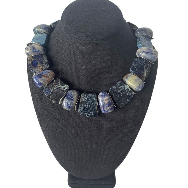 Zacatecas Necklace Where ancient stone meets modern elegance. This striking necklace blends flat Imperial Jasper with oval Sodalite stones, interspersed with gleaming silver spacer beads. The palette is a symphony of blues—deep navy, misty gray, and soft sky tones—each stone revealing its own marbled story. Measuring 18 inches with an extender reaching up to 22 inches, and weighing 8 ounces, it offers a substantial yet graceful presence around the neck. Imperial Jasper is revered for its grounding energy and intricate veining. The variety featured here hails from the rugged terrain of Zacatecas, Mexico, a region known for its rich deposits of semiprecious stones. Nestled in the Sierra Madre Occidental, Zacatecas has been a source of mineral beauty for centuries, with Imperial Jasper prized for its durability and spiritual symbolism. Sodalite, with its celestial blue hues, complements the Jasper’s earthy elegance, adding depth and contrast. Together, they create a piece that feels both ancient and contemporary—a wearable tribute to the artistry of nature and the legacy of Zacatecas. Whether paired with linen or leather, this necklace commands attention. It’s not just jewelry—it’s a journey through stone, history, and the soul of Zacatecas. Let its blues speak for you, three times over.