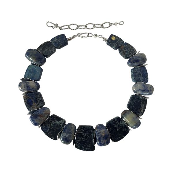 Zacatecas Necklace Where ancient stone meets modern elegance. This striking necklace blends flat Imperial Jasper with oval Sodalite stones, interspersed with gleaming silver spacer beads. The palette is a symphony of blues—deep navy, misty gray, and soft sky tones—each stone revealing its own marbled story. Measuring 18 inches with an extender reaching up to 22 inches, and weighing 8 ounces, it offers a substantial yet graceful presence around the neck. Imperial Jasper is revered for its grounding energy and intricate veining. The variety featured here hails from the rugged terrain of Zacatecas, Mexico, a region known for its rich deposits of semiprecious stones. Nestled in the Sierra Madre Occidental, Zacatecas has been a source of mineral beauty for centuries, with Imperial Jasper prized for its durability and spiritual symbolism. Sodalite, with its celestial blue hues, complements the Jasper’s earthy elegance, adding depth and contrast. Together, they create a piece that feels both ancient and contemporary—a wearable tribute to the artistry of nature and the legacy of Zacatecas. Whether paired with linen or leather, this necklace commands attention. It’s not just jewelry—it’s a journey through stone, history, and the soul of Zacatecas. Let its blues speak for you, three times over.