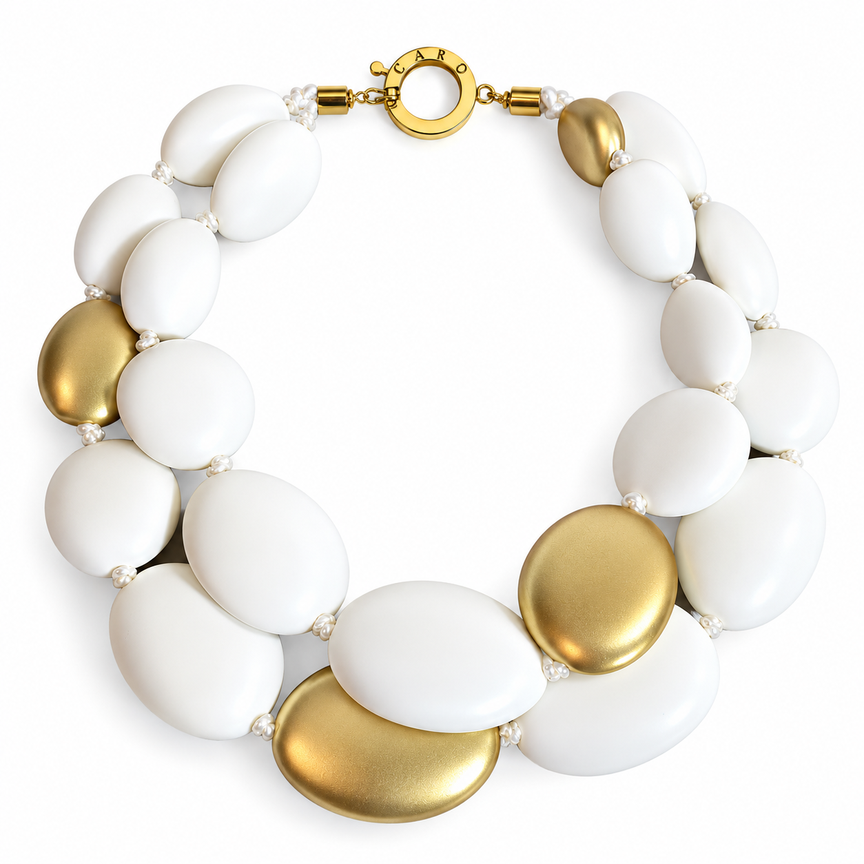 Double-strand necklace composed of large, smooth oval beads in matte white and metallic gold tones. The beads are arranged in an alternating pattern, creating a sculptural, pebble-like silhouette. The necklace is secured with a round gold clasp and displayed on a neutral fabric background.