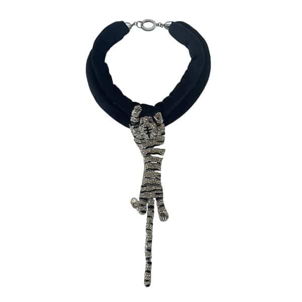 Bengal Tiger Necklace 0369222 A dramatic blend of texture, symbolism, and sculptural detail defines this necklace, designed around two strands of extra‑soft velvet cord and a rhinestone‑encrusted Bengal Tiger that appears to grip the cords with lifelike strength. The plush velvet creates a smooth, matte foundation, while the crystal‑studded tiger adds brilliant contrast, giving the piece a luxurious interplay of softness and shine. Measuring 20 inches in length and weighing 6 ounces, it drapes comfortably while maintaining a bold, commanding presence on the neckline. Design and Materials Two velvet strands that feel gentle against the skin Rhinestone Bengal Tiger centerpiece with sculpted paws and detailed striping 20-inch length, ideal for statement layering 6-ounce weight for a substantial yet wearable feel Cultural and Mythological Significance In Hindu mythology, the tiger is the divine mount (vahana) of Goddess Durga, symbolizing courage, protection, and the triumph of righteous power. Durga riding a tiger represents fearless determination and the ability to overcome obstacles with grace. Incorporating this imagery, the necklace becomes more than an accessory—it becomes a wearable emblem of strength, resilience, and spiritual guardianship. Style Impact The contrast of velvet and rhinestones creates a striking visual rhythm, making this piece ideal for collectors, fashion enthusiasts, and anyone drawn to jewelry with story and presence. It pairs effortlessly with minimalist outfits or adds edge to evening wear.