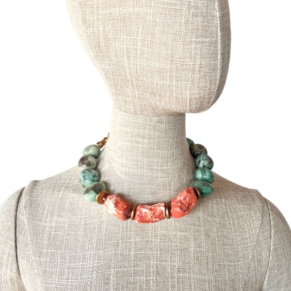 Truth Necklace Where color speaks and meaning resonates. This handcrafted necklace pairs the serene elegance of natural amazonite with the fiery vibrance of orange coral, creating a striking balance of calm and vitality. Measuring 18 inches with an extender reaching 23, it drapes gracefully across the collarbone, offering both comfort and presence at just 8 ounces. Amazonite, often called the “stone of truth,” is cherished for its soothing energy and its association with clarity, honesty, and heartfelt communication. Its greenish-blue hues evoke tranquil waters and open skies—an invitation to speak with authenticity and listen with compassion. At the center, bold coral beads add warmth and contrast, echoing the pulse of creativity and life force. Between each stone, natural coconut spacer beads lend an earthy texture and organic rhythm, grounding the piece in nature’s quiet wisdom. A decorative clasp with gold-toned accents completes the design with refined detail. Truth is not just a word—it’s a way of being. This necklace honors that principle, encouraging the wearer to embrace their voice, their story, their essence. Whether worn as a personal talisman or a statement accessory, it carries a quiet power that transcends trends. Truth in color. Truth in craftsmanship. Truth in you. Let this piece be your reminder to live and speak with intention.