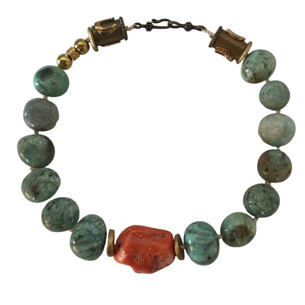 Amazon Necklace Rooted in nature. Radiant in spirit. This necklace is a tribute to the quiet power of simplicity. Crafted with natural amazonite beads in soft green-blue tones, it evokes the lush tranquility of riverbeds and forest canopies. At its heart lies a single coral stone—bold, warm, and unmistakably alive—anchoring the piece with a pulse of vibrant energy. Amazonite, known as the “stone of truth,” is celebrated for its calming influence and its ability to inspire honest expression. Its gentle hues mirror the serenity of the Amazon’s flowing waters, inviting clarity and emotional balance. The necklace’s 18-inch length, extendable to 23 inches, offers graceful drape and versatility, while its 8-ounce weight ensures a substantial yet comfortable presence. Natural coconut spacer beads add an earthy rhythm between the stones, enhancing the organic harmony of the design. A decorative clasp with gold-toned accents completes the look with artisanal finesse. Amazon is more than a name—it’s a feeling, a force, a connection to the wild and the wise. This necklace channels that essence, offering a wearable reminder of strength in softness and truth in simplicity. Let it be your companion in moments of reflection, expression, and quiet confidence.