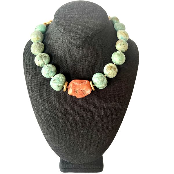 Amazon Necklace Rooted in nature. Radiant in spirit. This necklace is a tribute to the quiet power of simplicity. Crafted with natural amazonite beads in soft green-blue tones, it evokes the lush tranquility of riverbeds and forest canopies. At its heart lies a single coral stone—bold, warm, and unmistakably alive—anchoring the piece with a pulse of vibrant energy. Amazonite, known as the “stone of truth,” is celebrated for its calming influence and its ability to inspire honest expression. Its gentle hues mirror the serenity of the Amazon’s flowing waters, inviting clarity and emotional balance. The necklace’s 18-inch length, extendable to 23 inches, offers graceful drape and versatility, while its 8-ounce weight ensures a substantial yet comfortable presence. Natural coconut spacer beads add an earthy rhythm between the stones, enhancing the organic harmony of the design. A decorative clasp with gold-toned accents completes the look with artisanal finesse. Amazon is more than a name—it’s a feeling, a force, a connection to the wild and the wise. This necklace channels that essence, offering a wearable reminder of strength in softness and truth in simplicity. Let it be your companion in moments of reflection, expression, and quiet confidence.