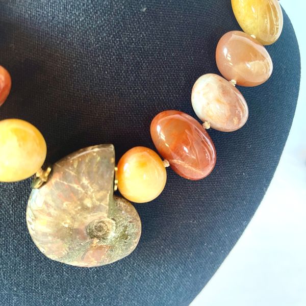 Fossil Necklace Ancient form. Modern radiance. Earth‑born elegance. This striking necklace honors the quiet power of deep time, centered around a beautifully preserved ammonite whose spiraling chambers reveal the mineral artistry of the natural world. Over millions of years, layers of aragonite, calcite, and iron-rich sediments transformed the original shell into a captivating Fossil with intricate patterns and earthy tones that feel both ancient and alive. Highly polished Aventurine beads frame the centerpiece, their warm, luminous hues adding a gentle shimmer that complements the ammonite’s organic geometry. Known for its subtle sparkle and grounding energy, Aventurine brings a refined glow to the design, enhancing its natural sophistication. Measuring 18 inches with an extender reaching 23, the necklace offers a customizable drape, while its 8‑ounce weight provides a satisfying, substantial presence. Each bead and curve reflects the slow, patient work of nature—pressure, heat, and mineral infusion shaping what was once a living creature into a treasured Fossil. The result is a piece that feels both timeless and contemporary, a wearable reminder of Earth’s evolving story. This necklace invites admiration, sparks conversation, and carries the quiet strength of transformation. Let the ammonite’s spiral draw the eye, let the Aventurine glow softly against your skin, and let the ancient beauty of this Fossil accompany you wherever you go.
