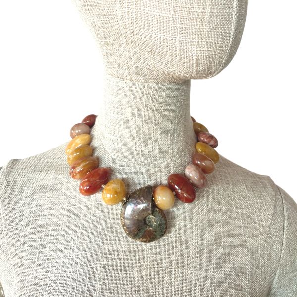 Fossil Necklace Ancient form. Modern radiance. Earth‑born elegance. This striking necklace honors the quiet power of deep time, centered around a beautifully preserved ammonite whose spiraling chambers reveal the mineral artistry of the natural world. Over millions of years, layers of aragonite, calcite, and iron-rich sediments transformed the original shell into a captivating Fossil with intricate patterns and earthy tones that feel both ancient and alive. Highly polished Aventurine beads frame the centerpiece, their warm, luminous hues adding a gentle shimmer that complements the ammonite’s organic geometry. Known for its subtle sparkle and grounding energy, Aventurine brings a refined glow to the design, enhancing its natural sophistication. Measuring 18 inches with an extender reaching 23, the necklace offers a customizable drape, while its 8‑ounce weight provides a satisfying, substantial presence. Each bead and curve reflects the slow, patient work of nature—pressure, heat, and mineral infusion shaping what was once a living creature into a treasured Fossil. The result is a piece that feels both timeless and contemporary, a wearable reminder of Earth’s evolving story. This necklace invites admiration, sparks conversation, and carries the quiet strength of transformation. Let the ammonite’s spiral draw the eye, let the Aventurine glow softly against your skin, and let the ancient beauty of this Fossil accompany you wherever you go.
