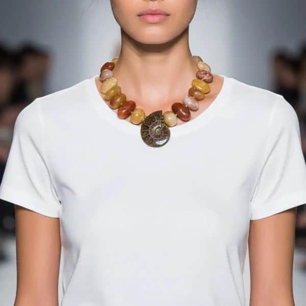 Fossil Necklace Ancient form. Modern radiance. Earth‑born elegance. This striking necklace honors the quiet power of deep time, centered around a beautifully preserved ammonite whose spiraling chambers reveal the mineral artistry of the natural world. Over millions of years, layers of aragonite, calcite, and iron-rich sediments transformed the original shell into a captivating Fossil with intricate patterns and earthy tones that feel both ancient and alive. Highly polished Aventurine beads frame the centerpiece, their warm, luminous hues adding a gentle shimmer that complements the ammonite’s organic geometry. Known for its subtle sparkle and grounding energy, Aventurine brings a refined glow to the design, enhancing its natural sophistication. Measuring 18 inches with an extender reaching 23, the necklace offers a customizable drape, while its 8‑ounce weight provides a satisfying, substantial presence. Each bead and curve reflects the slow, patient work of nature—pressure, heat, and mineral infusion shaping what was once a living creature into a treasured Fossil. The result is a piece that feels both timeless and contemporary, a wearable reminder of Earth’s evolving story. This necklace invites admiration, sparks conversation, and carries the quiet strength of transformation. Let the ammonite’s spiral draw the eye, let the Aventurine glow softly against your skin, and let the ancient beauty of this Fossil accompany you wherever you go.