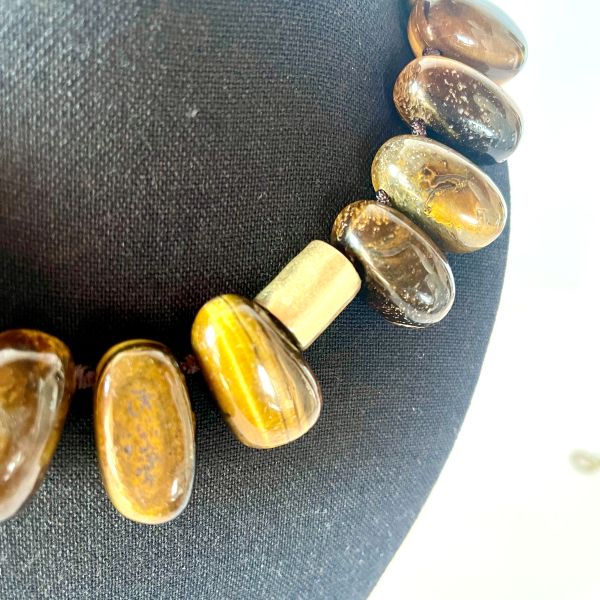 Taurus Necklace Earthy presence. Grounded elegance. Natural strength. This bold necklace is crafted from large, polished beads in warm, earthy tones that echo the steady, grounded nature of the Taurus spirit. Each bead carries its own organic striations and depth, creating a rich landscape of browns, ambers, and golden hues.  Cylindrical accent pieces add contrast and structure, giving the design a refined, architectural rhythm. Measuring 16 inches with an extender reaching 22, the necklace offers a versatile fit that sits beautifully along the neckline. Its 10‑ounce weight gives it a substantial, confident feel—perfect for those who appreciate jewelry with presence and intention. Taurus is known for its connection to the earth, its love of natural beauty, and its steady, loyal energy. This piece reflects those qualities through its grounded palette and its emphasis on natural materials. The warm tones evoke stability and comfort, while the polished finish adds a touch of sensuality that aligns with Taurus’s Venus‑ruled appreciation for tactile luxury. Whether worn as a statement of personal strength or simply as a striking accessory, this necklace brings warmth, balance, and a sense of rooted elegance to any look.