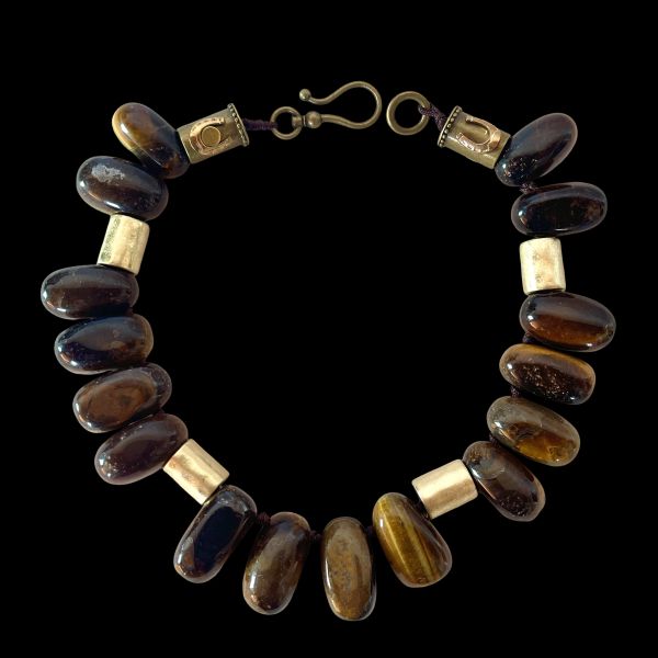 Taurus Necklace Earthy presence. Grounded elegance. Natural strength. This bold necklace is crafted from large, polished beads in warm, earthy tones that echo the steady, grounded nature of the Taurus spirit. Each bead carries its own organic striations and depth, creating a rich landscape of browns, ambers, and golden hues.  Cylindrical accent pieces add contrast and structure, giving the design a refined, architectural rhythm. Measuring 16 inches with an extender reaching 22, the necklace offers a versatile fit that sits beautifully along the neckline. Its 10‑ounce weight gives it a substantial, confident feel—perfect for those who appreciate jewelry with presence and intention. Taurus is known for its connection to the earth, its love of natural beauty, and its steady, loyal energy. This piece reflects those qualities through its grounded palette and its emphasis on natural materials. The warm tones evoke stability and comfort, while the polished finish adds a touch of sensuality that aligns with Taurus’s Venus‑ruled appreciation for tactile luxury. Whether worn as a statement of personal strength or simply as a striking accessory, this necklace brings warmth, balance, and a sense of rooted elegance to any look.