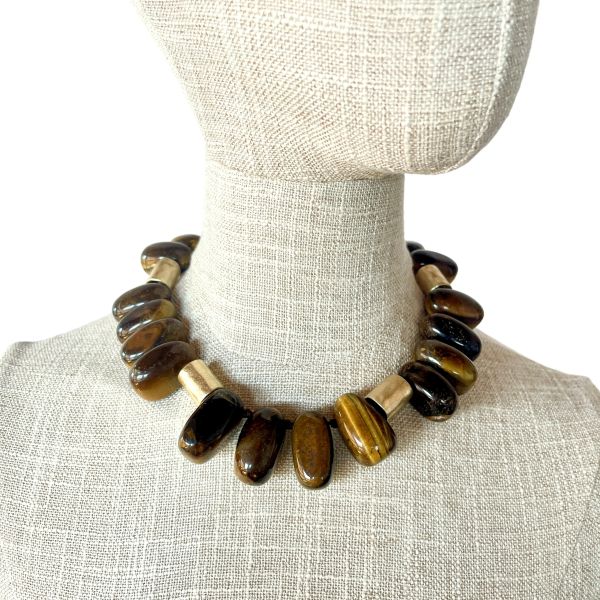 Taurus Necklace Earthy presence. Grounded elegance. Natural strength. This bold necklace is crafted from large, polished beads in warm, earthy tones that echo the steady, grounded nature of the Taurus spirit. Each bead carries its own organic striations and depth, creating a rich landscape of browns, ambers, and golden hues.  Cylindrical accent pieces add contrast and structure, giving the design a refined, architectural rhythm. Measuring 16 inches with an extender reaching 22, the necklace offers a versatile fit that sits beautifully along the neckline. Its 10‑ounce weight gives it a substantial, confident feel—perfect for those who appreciate jewelry with presence and intention. Taurus is known for its connection to the earth, its love of natural beauty, and its steady, loyal energy. This piece reflects those qualities through its grounded palette and its emphasis on natural materials. The warm tones evoke stability and comfort, while the polished finish adds a touch of sensuality that aligns with Taurus’s Venus‑ruled appreciation for tactile luxury. Whether worn as a statement of personal strength or simply as a striking accessory, this necklace brings warmth, balance, and a sense of rooted elegance to any look.