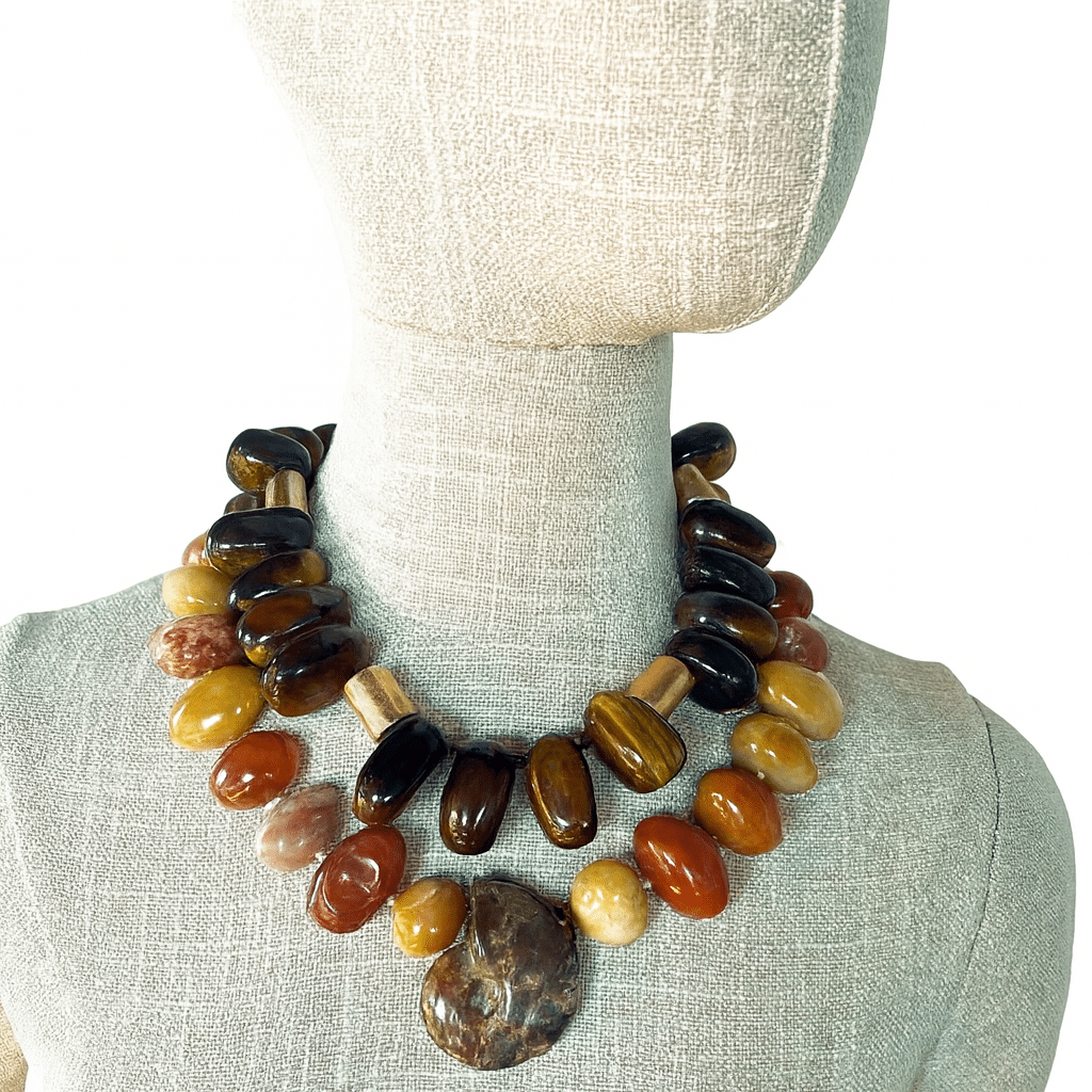 Tiger Eye & Aventurine Ammonite Combo Earthbound elegance. Ancient energy. Layered strength. This striking duo—products 0369244 and 0369245—offers a powerful fusion of natural elements and timeless design. Crafted with polished Tiger Eye and Aventurine stones, each necklace showcases the grounding warmth of golden-brown hues. Antique gold accent beads thread through both strands, adding a touch of vintage refinement and enhancing the organic richness of the stones. At the heart of this combo lies a dramatic Ammonite pendant—an ancient fossil spiral that evokes transformation, endurance, and the rhythm of nature. Its marbled pattern and bold presence anchor the layered look with symbolic weight and visual intrigue. Each necklace measures 18 inches in length, designed to sit gracefully at the collarbone, and together they weigh a substantial 17 ounces—luxurious yet wearable. Whether worn as a layered statement or styled individually, these pieces offer versatility and impact. You may choose to purchase each necklace separately to suit your styling needs, or opt for the Tiger Eye & Aventurine Ammonite Combo at a special bundled price. Either way, you’re investing in a piece that speaks to strength, serenity, and the beauty of natural design.