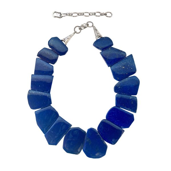 Asymmetric Lapis Elegance Necklace A deep‑blue statement shaped by history, artistry, and the Earth’s own palette. This captivating necklace is crafted from natural lapis stones, each one shaped into an asymmetric, flat form that highlights the mineral’s raw beauty. The deep celestial blues, touched with subtle golden specks, create a visual rhythm that feels both ancient and contemporary. Designed to rest gracefully along the neckline, the piece offers a bold yet refined presence—perfect for those who appreciate jewelry with character and story. Lapis has been treasured for over 6,000 years, admired by civilizations from Mesopotamia to Egypt. Cleopatra famously used powdered lapis as eyeshadow, and artisans of the Renaissance ground it into ultramarine pigment, once more valuable than gold. Its rich color and symbolic associations with wisdom, truth, and inner vision have made it one of the world’s most enduring gemstones. The natural variations in each stone ensure that no two necklaces are ever alike. With its striking silhouette and thoughtful composition, this necklace transforms the timeless beauty of Lazuli into a wearable work of art. Whether paired with everyday attire or reserved for special occasions, it brings forward a sense of depth, elegance, and ancient allure.
