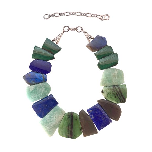 Multistone Harmony Necklace A celebration of Earth’s colors, textures, and ancient stories. This striking necklace brings together a curated ensemble of flat-cut Malachite, Lapis Lazuli, Labradorite, Nephrite, and Jadeite—each stone chosen for its natural beauty and its unique place in the world’s mineral heritage. The interplay of deep greens, oceanic blues, and iridescent grays creates a fluid, organic rhythm that feels both grounded and luminous. Measuring 15 to 20 inches with an adjustable extender and weighing 9 ounces, the piece drapes with a satisfying presence while remaining comfortable for all-day wear. Among these stones, Nephrite holds a special connection to Pounamu, the treasured greenstone of the Māori people of Aotearoa New Zealand. Historically, Pounamu was used not only for adornment but also for tools, weapons, and heirlooms passed down through generations. Its cultural significance is so profound that certain varieties of Pounamu were considered symbols of authority and guardianship. The combination of these storied stones transforms the necklace into more than an accessory—it becomes a wearable tapestry of geology, culture, and artistry. Each bead carries its own quiet power, and together they create a piece that feels timeless, expressive, and deeply connected to the natural world.