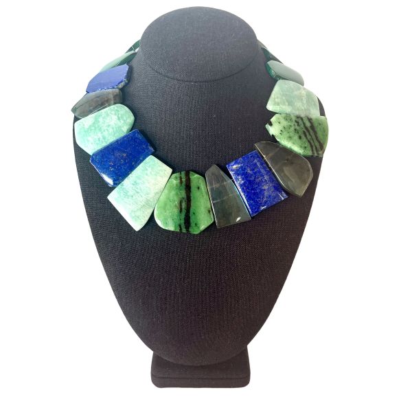 Multistone Harmony Necklace A celebration of Earth’s colors, textures, and ancient stories. This striking necklace brings together a curated ensemble of flat-cut Malachite, Lapis Lazuli, Labradorite, Nephrite, and Jadeite—each stone chosen for its natural beauty and its unique place in the world’s mineral heritage. The interplay of deep greens, oceanic blues, and iridescent grays creates a fluid, organic rhythm that feels both grounded and luminous. Measuring 15 to 20 inches with an adjustable extender and weighing 9 ounces, the piece drapes with a satisfying presence while remaining comfortable for all-day wear. Among these stones, Nephrite holds a special connection to Pounamu, the treasured greenstone of the Māori people of Aotearoa New Zealand. Historically, Pounamu was used not only for adornment but also for tools, weapons, and heirlooms passed down through generations. Its cultural significance is so profound that certain varieties of Pounamu were considered symbols of authority and guardianship. The combination of these storied stones transforms the necklace into more than an accessory—it becomes a wearable tapestry of geology, culture, and artistry. Each bead carries its own quiet power, and together they create a piece that feels timeless, expressive, and deeply connected to the natural world.
