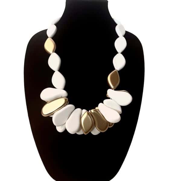 ***Free Spirited Short 0369254*** Inspired by freedom, this necklace embodies the essence of a Free Spirited Short—unbound, expressive, and beautifully bold. Crafted from smooth matte white beads, its design is elevated by a cluster of high‑shine gold accents that catch the light with every movement. The contrast between the soft, matte finish of the white beads and the reflective brilliance of the gold creates a striking balance of calm and radiance. Measuring 27 inches in length and weighing 11 ounces, this piece offers a substantial yet comfortable presence. Its sculptural silhouette draws the eye to the center, where the gold cluster forms a focal point reminiscent of sunlit pebbles gathered along a shoreline. The necklace drapes gracefully across the chest, making it an ideal statement piece for both casual and elevated styling. Whether paired with natural linens, crisp cottons, or evening textures, this necklace adds a touch of organic elegance to any look. Its clean lines and warm metallic accents make it versatile enough for everyday wear while still delivering the impact of a gallery‑worthy accessory. A piece for those who move with intention and embrace beauty in simplicity, it stands as a reminder that style can be both grounded and luminous. See it paired with product 0369255 Free Spirited Long, sold separately.