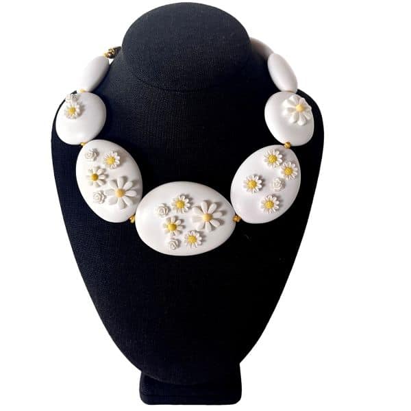 **Spring 0369258 – White Floral Appliqué Choker Necklace** Soft, sculptural elegance defines *Spring 0369258*, a short choker‑length necklace designed to rest gracefully along the neckline. Large matte white oval beads form a clean, modern foundation, each adorned with delicate white appliqué flowers that lend a touch of handcrafted charm. The floral details feature subtle yellow centers, and the necklace is strung on a coordinating yellow cord that enhances the design’s warm, sunny character while adding a subtle pop of color. The gentle palette and botanical accents evoke the freshness and renewal associated with **Spring**, making this piece a standout accessory for any season. Measuring 19 inches with an extender that allows up to 23 inches, the necklace offers a flexible fit that adapts easily to different necklines and styling preferences. At just 6 ounces, it is comfortable and lightweight yet maintains a bold visual presence. The matte finish of the beads gives the necklace a refined, contemporary look, while the appliqué flowers introduce texture and artistry. The combination of white and gold-toned spacers with the yellow cord creates a harmonious balance that feels both playful and sophisticated. This design captures the gentle optimism of **Spring**, making it an ideal choice for anyone who loves jewelry that blends simplicity, craftsmanship, and a touch of whimsy. The thoughtful details and soft floral motif ensure that **Spring** 0369258 becomes a cherished addition to any collection.