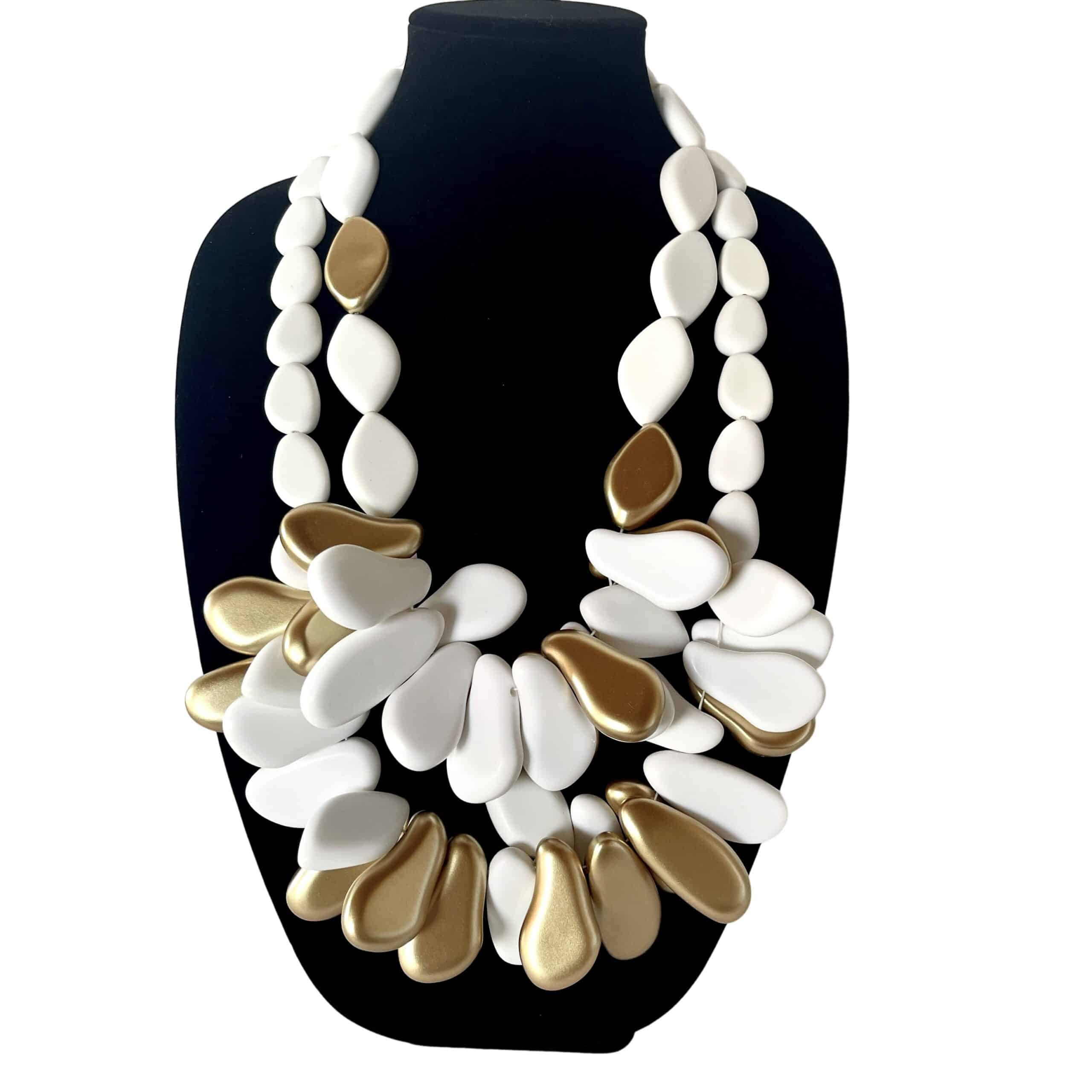 Inspired by freedom, this necklace embodies the essence of a Free Spirited — unbound, expressive, and beautifully bold. Crafted from smooth matte white beads, its design is elevated by a cluster of high‑shine gold accents that catch the light with every movement. The contrast between the soft, matte finish of the white beads and the reflective brilliance of the gold creates a striking balance of calm and radiance. The Free Spirited Combo's longest strand measures 33 inches and weighs 14 ounces, while the shorter strand measures 27 inches and weighs 11 ounces. The combined weight for both strands is 25 ounces. The Free Spirited Combo offers a substantial yet comfortable presence. Its sculptural silhouette draws the eye toward the center, where the gold cluster forms a focal point reminiscent of sunlit pebbles gathered along a shoreline. The necklace drapes gracefully across the chest, making it an ideal statement piece for both casual and elevated styling. Whether paired with natural linens, crisp cottons, or evening textures, this necklace adds a touch of organic elegance to any look. Its clean lines and warm metallic accents make it versatile enough for everyday wear while still delivering the impact of a gallery‑worthy accessory. A piece for those who move with intention and embrace beauty in simplicity, it stands as a reminder that style can be both grounded and luminous.