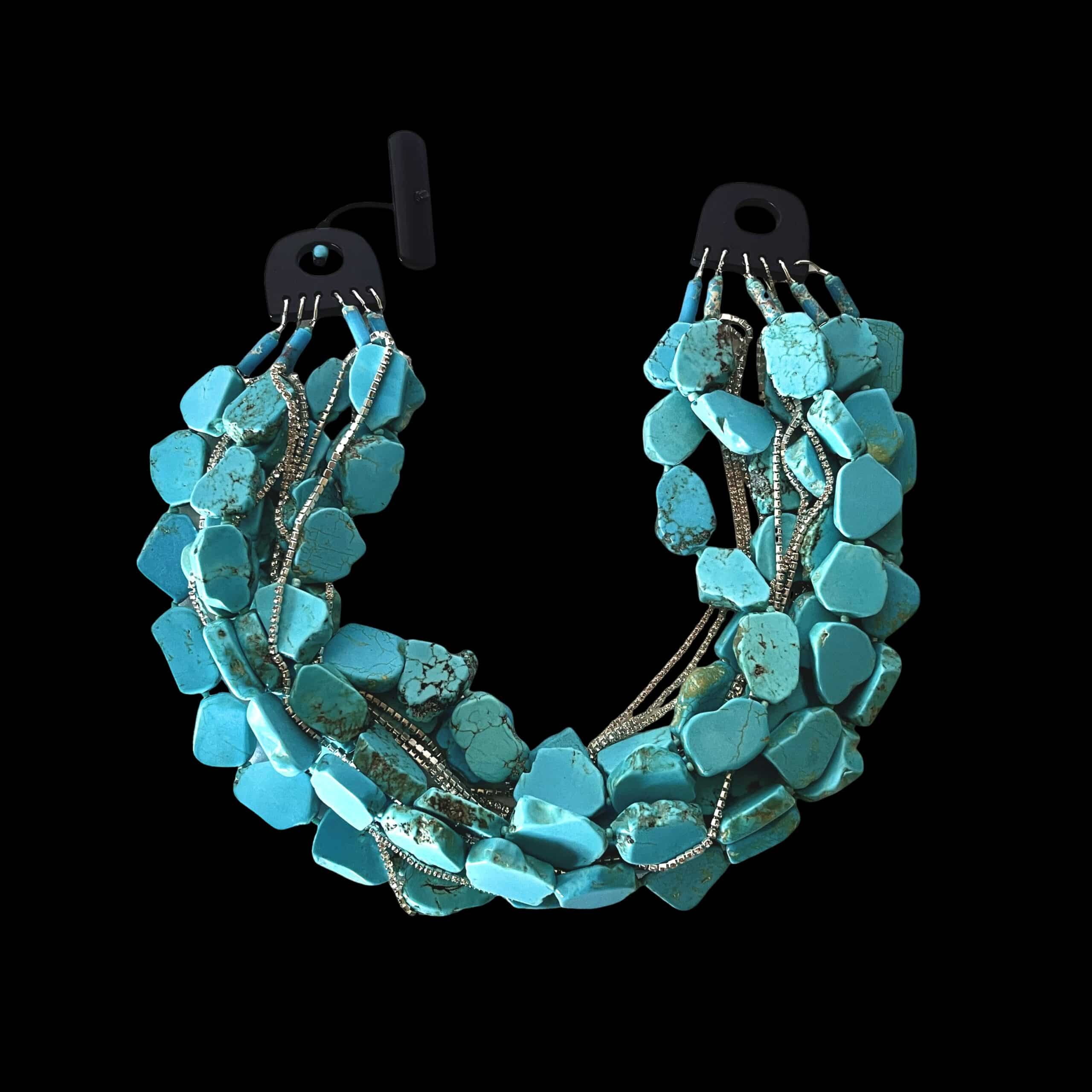 Make a bold statement with this multi-strand Tiel Chalcedony stone necklace, designed with rich texture, vibrant color, and elegant sparkle. The necklace features multiple strands of teal-colored chalcedony stones, each with a natural look that gives the piece depth and character. Strands of tiny Rhinestones are woven throughout, adding a delicate shimmer that beautifully complements the stones. Finished with a natural stone onyx toggle clasp, this necklace offers a refined contrast and a secure, stylish closure. Measuring 17 inches in length and weighing 18 ounces, it has a substantial feel while resting beautifully around the neckline. This Tiel Chalcedony necklace is perfect for dressing up a simple outfit or adding a unique finishing touch to evening wear. Its combination of natural stone, sparkle, and layered design makes it a standout piece for any jewelry collection. Chalcedony is a form of highly compacted quartz. 